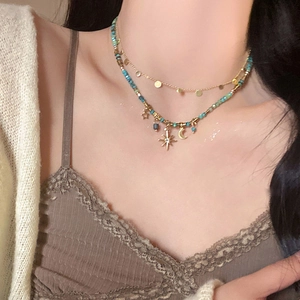 Detail of layered gold necklace with turquoise beads and celestial sun moon charms