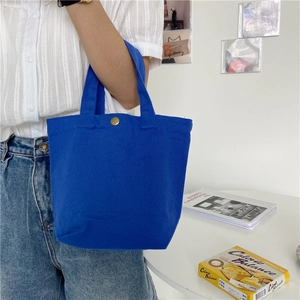 Navy blue canvas mini tote bag with gold button closure shown in a lifestyle scene