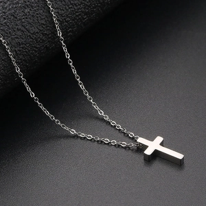 Polished silver stainless steel cross pendant necklace on a textured black background