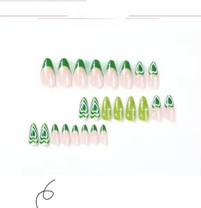 Detail view of oval press-on nails with green French tips and heart star patterns