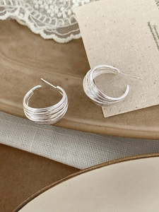 Detail shot of multi-layered silver C-shape earrings on a vintage aesthetic background