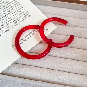 Macro detail of large translucent bright red resin C-shape hoop earrings on beige tray