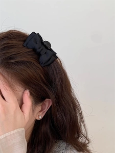 Vue latérale d'une petite pince à cheveux nœud en soie noire sur frange de femme