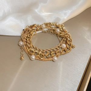 Detail of warm gold layered bracelet set with white pearls and OT buckle on silk