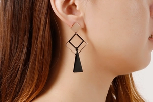 Detail view of champagne gold geometric drop earrings with black matte pendants worn by model