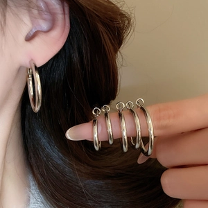 Detail showing five different sizes of polished silver hoop earrings on finger display