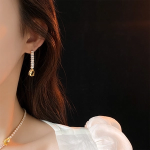 Detail of yellow teardrop zircon pendant and long earrings on a model with elegant lighting