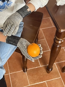 Detalle de guantes de punto a rayas blancas y negras sosteniendo una naranja fresca