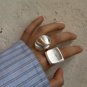 Macro detail of geometric silver brushed metal ring showing square and spherical elements