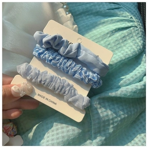 Three-piece set of blue fabric scrunchies including solid and striped patterns on a card