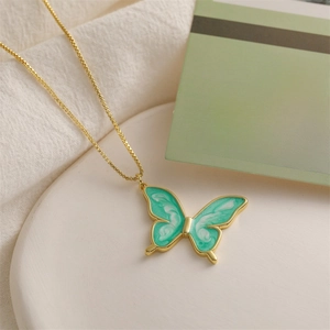 Macro detail of golden butterfly pendant with green enamel and fine box chain