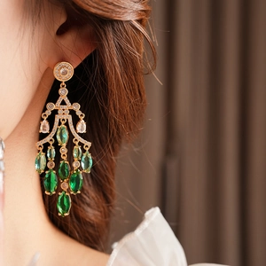 Close-up of gold tassel earrings with gradient green and white zircon stones on a model