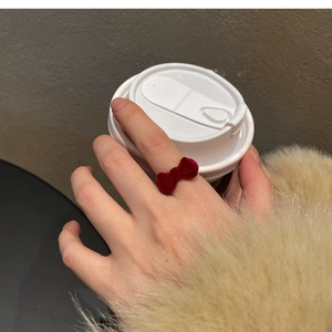 Detail of elegant red velvet bow open ring worn by model holding a white coffee cup