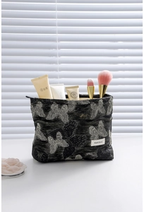 Close-up of black brocade makeup bag with white butterfly embroidery and zipper detail