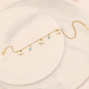 Detail of gold chain bracelet with white enamel clover and blue bead charms on marble