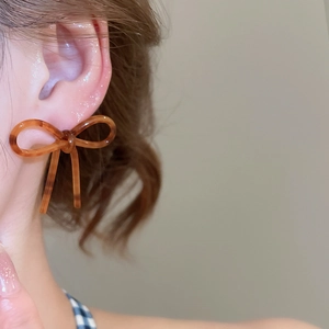 Gros plan d'un modèle portant des boucles d'oreilles nœud en résine ambrée brillante