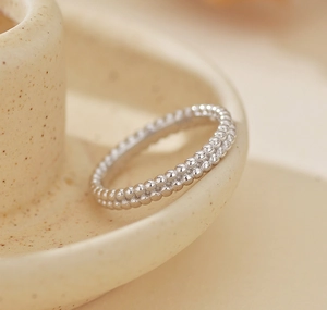 Macro detail of silver S925 minimalist double-row beaded band ring on ceramic dish