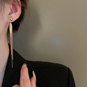 Close-up of golden long tassel earrings with sleek snake chain drop on a model