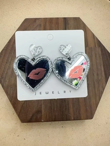 Detail of silver glitter heart earrings with lip motifs on a wooden display base