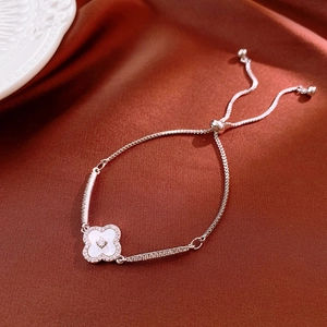 Macro detail of silver four-leaf clover bracelet with white pearl inlay on silk fabric