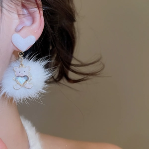 Detail of plush bear earring with heart stud and rhinestone accents on white fur ball