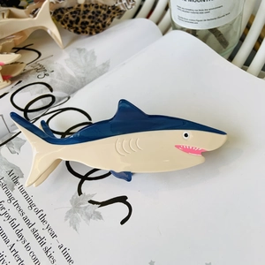 Blue and beige penguin shark hair claw clip made of acetate fiber on an open vintage book