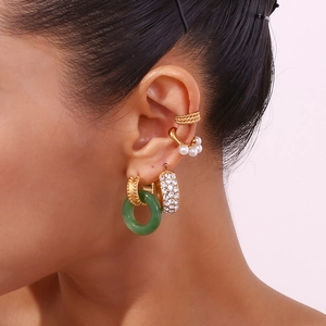 Close-up of gold layered earrings featuring green stone ring and pearl cuff details