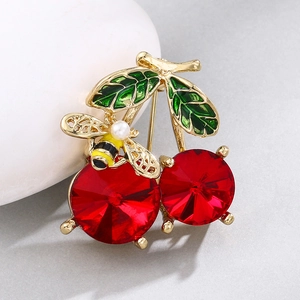 Macro shot of cherry brooch with red crystals, green enamel leaves and a small pearl bee