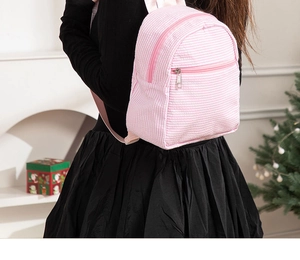 Model wearing a pink and white seersucker striped mini backpack with metal zippers