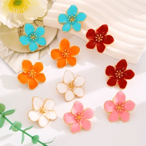 Makrofoto von bunten Emaille-Blumenohrringen mit goldenen Blüten auf weißem Tablett