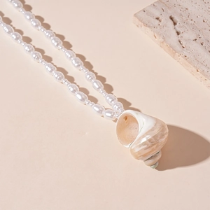 Detail of a pearl necklace featuring a natural seashell pendant on a beige stone