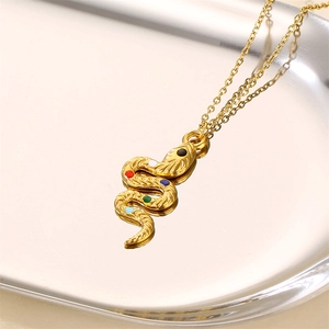 Golden snake pendant necklace with colorful gems on a glossy metal tray