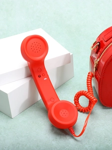 Retro red telephone-shaped handbag with classic receiver and spiral cord on white blocks
