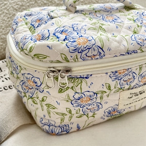 Detail of blue floral quilted makeup bag showing stitching texture and dual metal zippers