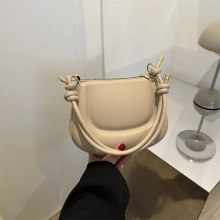 Dettaglio borsa in pelle beige con accento punto rosso e design del manico annodato