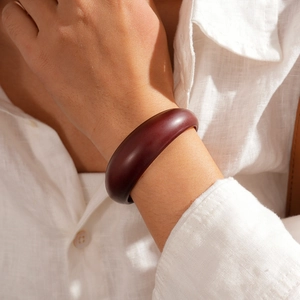Detail of a deep burgundy acrylic cuff bracelet on a model wearing white linen clothing