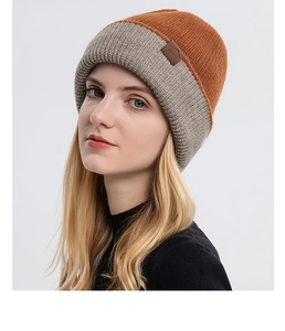 Detail of orange and light grey knit beanie featuring a brown leather mountain label patch