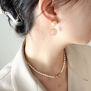 Elegant pearl necklace with pink pendant earrings set worn by a woman in beige blazer