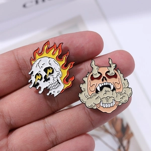 Detail view of two punk skull enamel pins with fire and smoke designs held in hand
