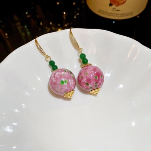 Detail of vintage style earrings with green and marble-patterned beads on a porcelain plate