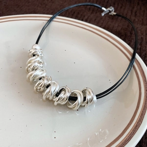 Detail of minimalist leather cord necklace with polished silver metal rings on ceramic tray