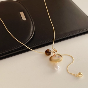 Detailed view of mushroom pendant and white pearl on gold chain necklace over black leather