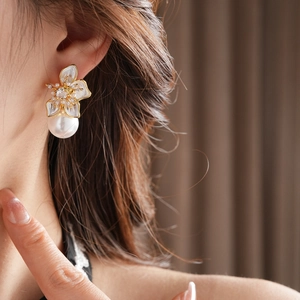 Detailed close-up of a white flower earring with a large pearl drop on a model