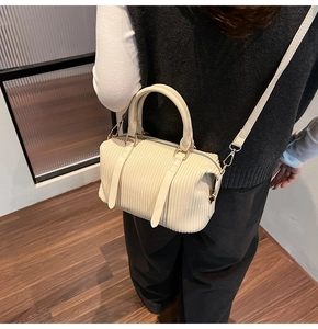 Detailansicht der cremefarbenen Rafftasche mit goldenen Beschlägen und abnehmbarem Gurt