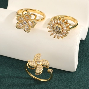 Golden rotating clover and sunflower rings set on green velvet, elegant fashion jewelry