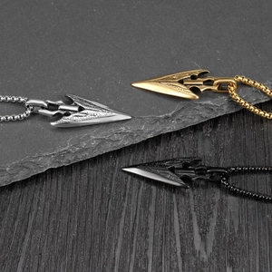 Arrowhead pendant necklaces in silver, gold, and black metal finishes on a textured dark wood