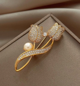 Macro detail of tulip brooch with golden metal, white zircons, and a soft yellow pearl
