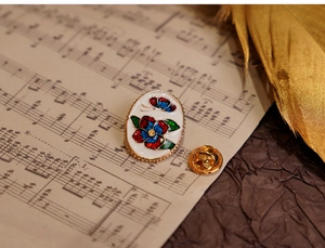 Detail of vintage flower enamel brooch pin on music sheet with golden feather