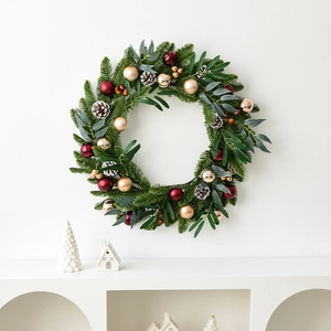 Classic Christmas wreath with red ornaments and pine cones on a white minimalist wall