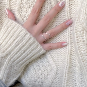 Close-up of minimalist 925 sterling silver wavy ring worn on finger with a knit background